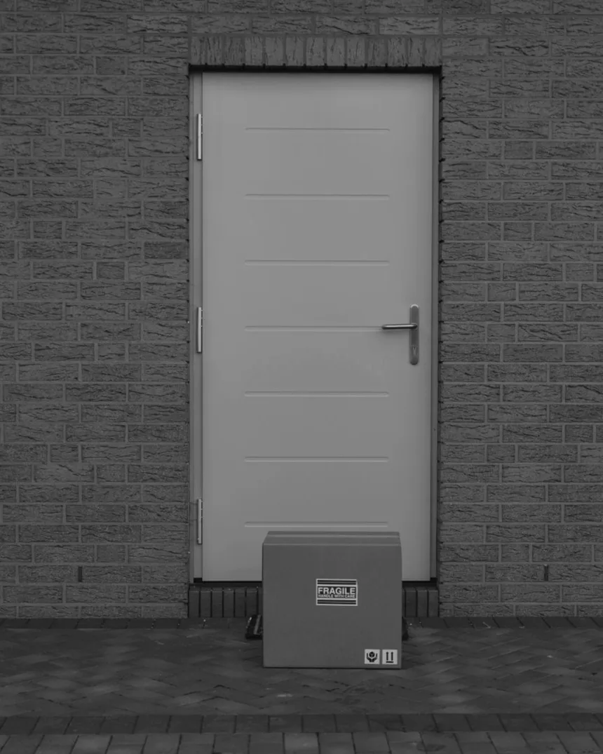 Un carton de livraison posé devant une porte blanche, sur un mur de brique.