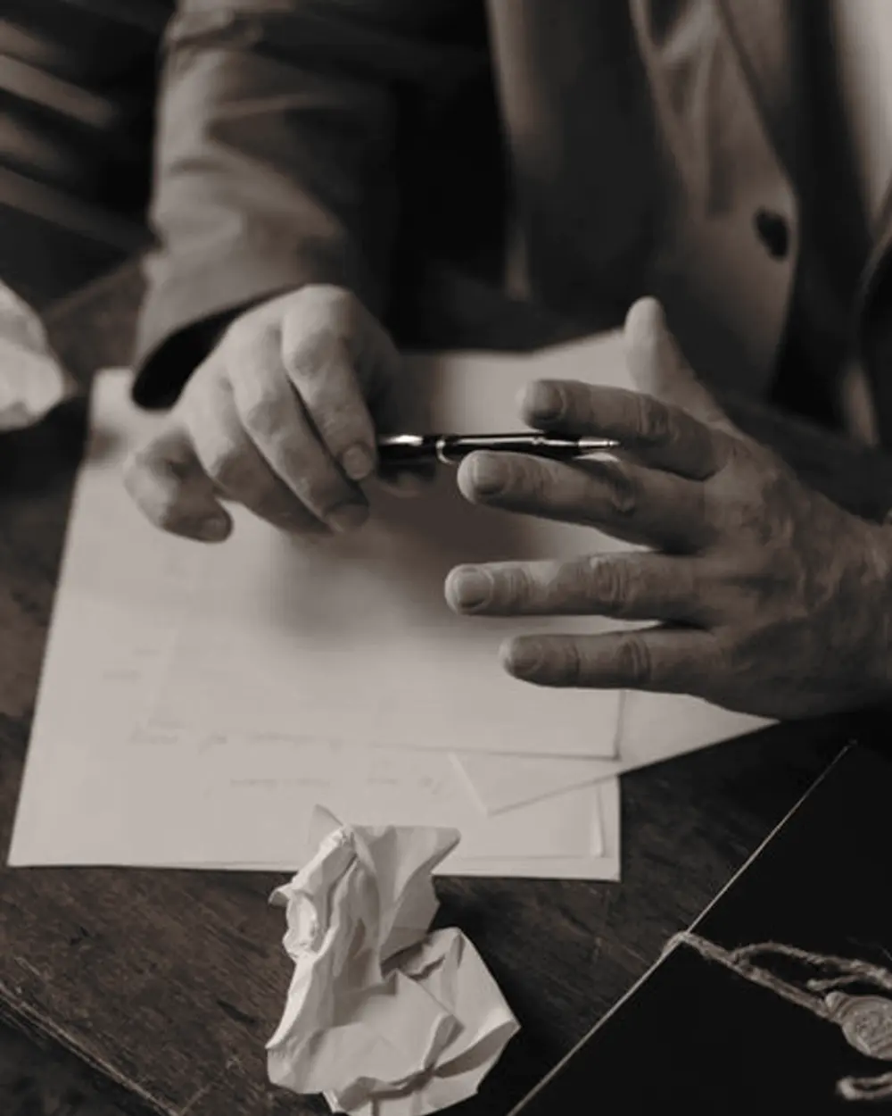 Deux mains au-dessus d'une feuille, un stylo, une page froissée.