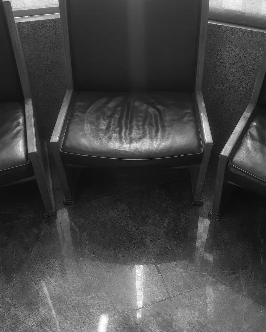 Trois fauteuils alignés dans une salle d'attente, au sol de pierre sombre.