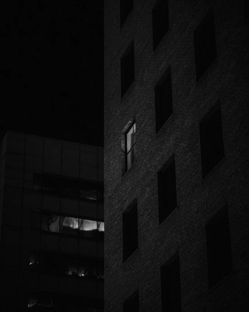 Une façade sombre la nuit, une seule fenêtre éclairée.