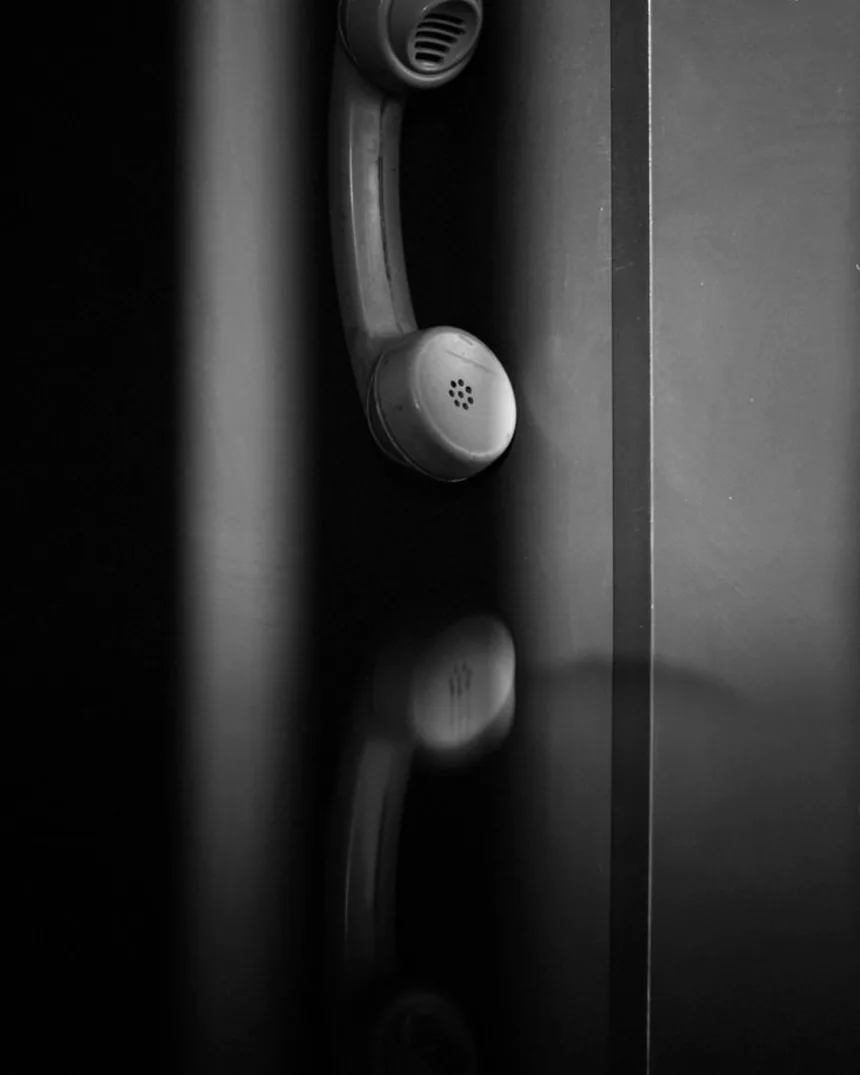 Un combiné téléphonique décroché, pendu le long d'une paroi sombre.